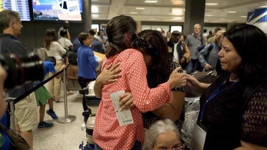 Two women hugging in a crowded airport terminal.