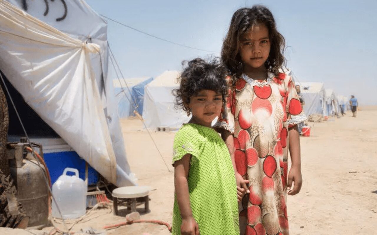 Two young girls standing in the sand near a tent.