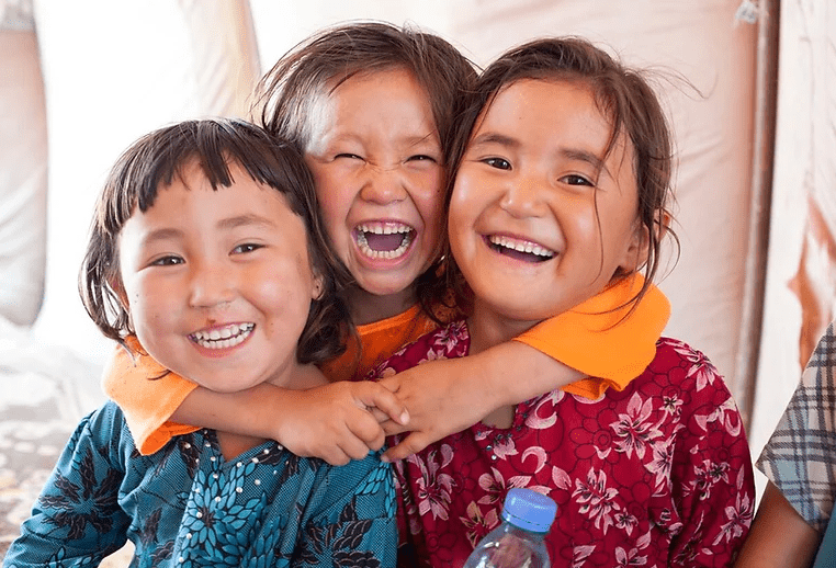 Three young girls are smiling and hugging each other.