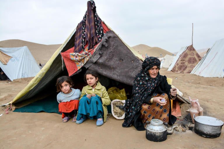 A woman and two children sitting in front of a tent.